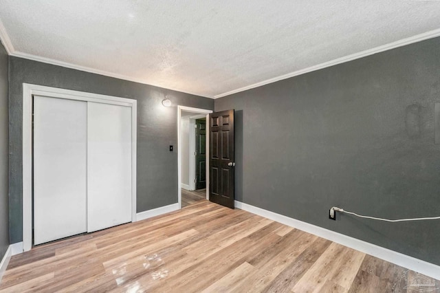 unfurnished bedroom with a textured ceiling, light wood-type flooring, crown molding, and a closet