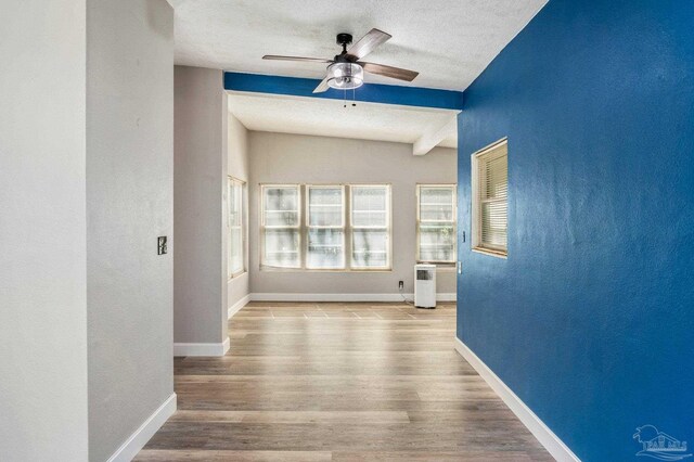 interior space featuring light wood-type flooring, a textured ceiling, lofted ceiling with beams, and ceiling fan