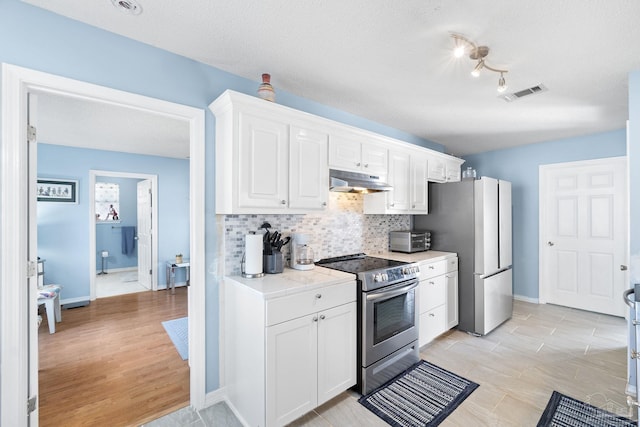 kitchen featuring under cabinet range hood, visible vents, white cabinets, appliances with stainless steel finishes, and decorative backsplash