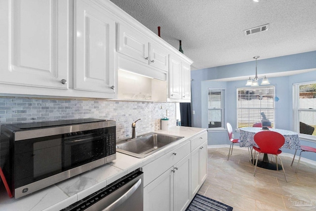 kitchen with a sink, visible vents, white cabinetry, backsplash, and stainless steel microwave