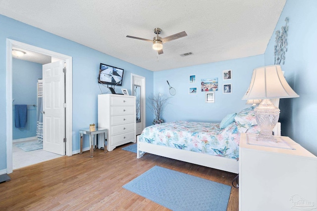 bedroom featuring a textured ceiling, ceiling fan, wood finished floors, visible vents, and baseboards