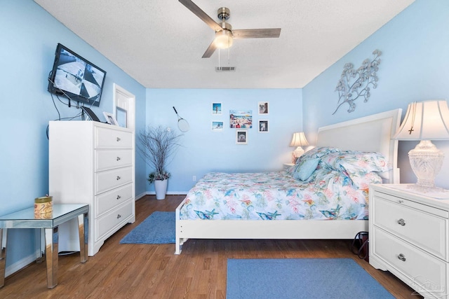 bedroom with a textured ceiling, wood finished floors, visible vents, and a ceiling fan