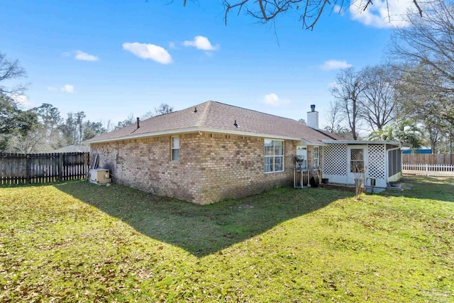 back of property with a shingled roof, a fenced backyard, a chimney, a yard, and brick siding