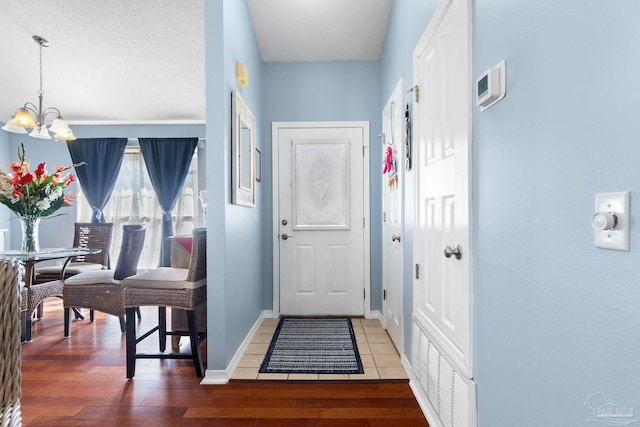 doorway with visible vents, an inviting chandelier, a textured ceiling, wood finished floors, and baseboards