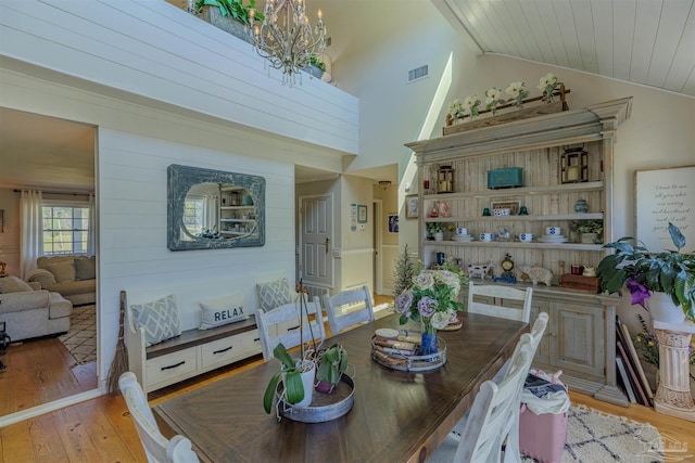dining area with visible vents, vaulted ceiling, a notable chandelier, and light wood finished floors