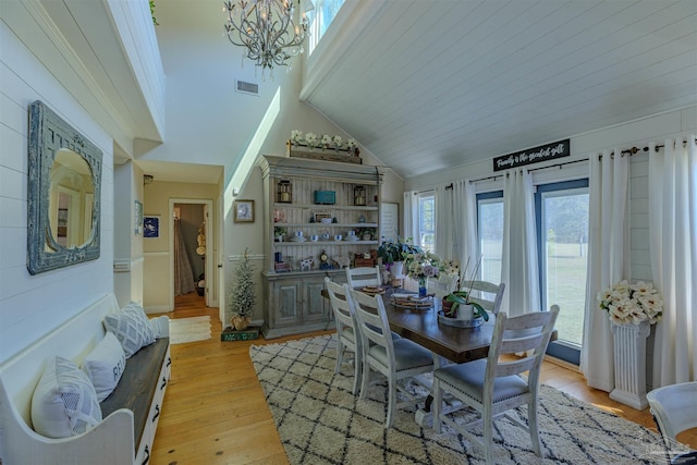 dining area featuring high vaulted ceiling, light wood-type flooring, visible vents, and a notable chandelier