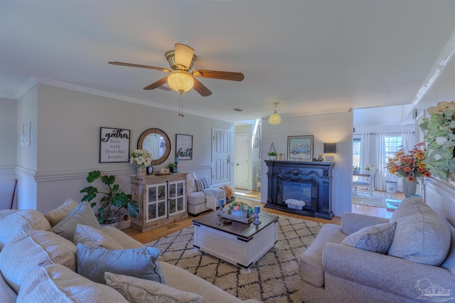living area featuring crown molding, a wainscoted wall, ceiling fan, a glass covered fireplace, and wood finished floors