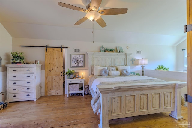 bedroom featuring light wood-style floors, a barn door, lofted ceiling, and visible vents