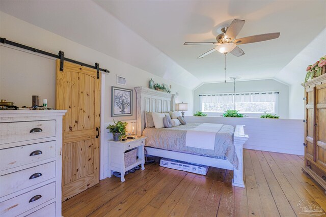 bedroom with visible vents, light wood finished floors, a ceiling fan, a barn door, and vaulted ceiling