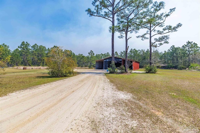 view of front of home featuring a pole building, a forest view, a front lawn, driveway, and an outdoor structure