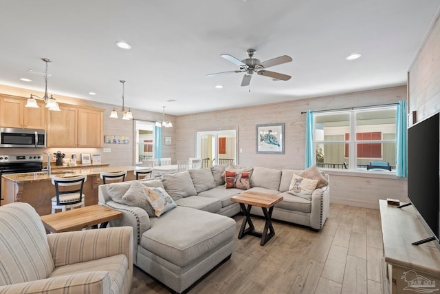 living room with ceiling fan with notable chandelier and light hardwood / wood-style floors