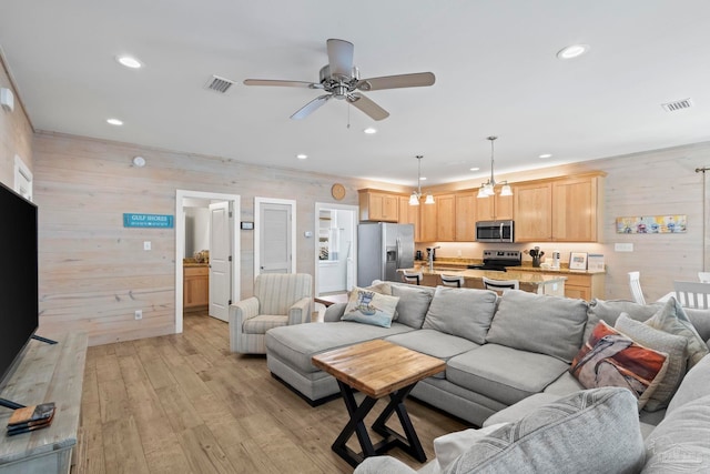 living room featuring wood walls, light hardwood / wood-style floors, and ceiling fan with notable chandelier