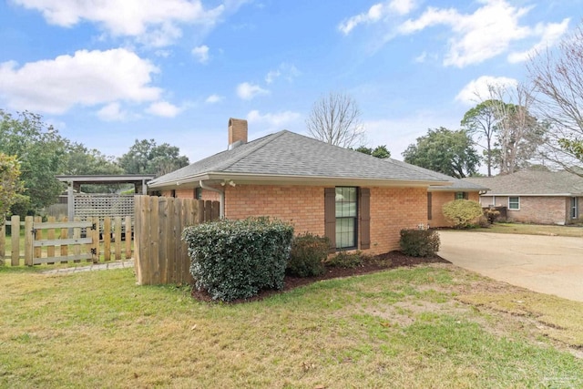 view of side of home with brick siding, a yard, a chimney, a shingled roof, and fence