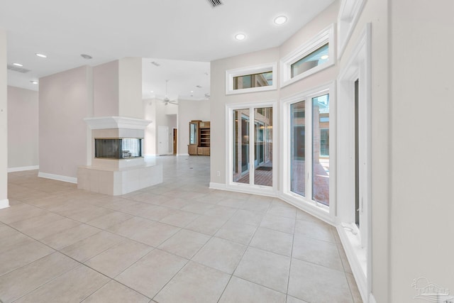 unfurnished living room featuring light tile patterned floors, recessed lighting, a high ceiling, baseboards, and a tiled fireplace