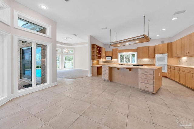 kitchen featuring light tile patterned floors, light countertops, backsplash, a kitchen island, and white appliances