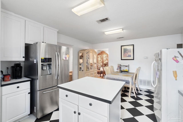 kitchen with white cabinetry, a kitchen island, stainless steel fridge, and white fridge