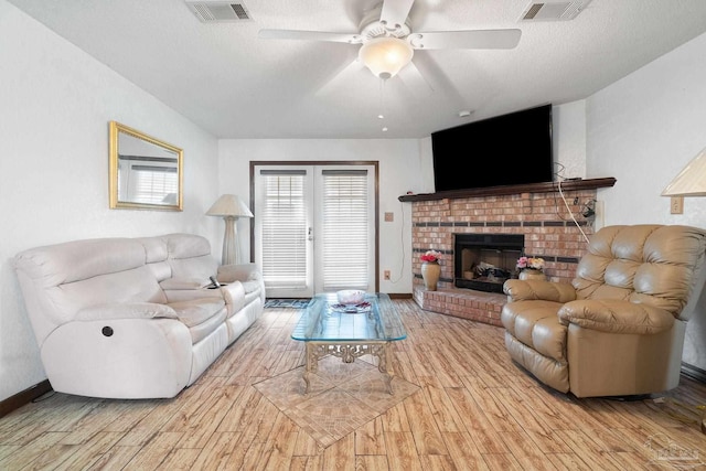 living room with light hardwood / wood-style flooring, ceiling fan, a textured ceiling, a brick fireplace, and french doors