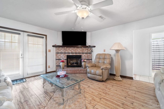 living room featuring light hardwood / wood-style flooring, ceiling fan, a textured ceiling, a brick fireplace, and french doors