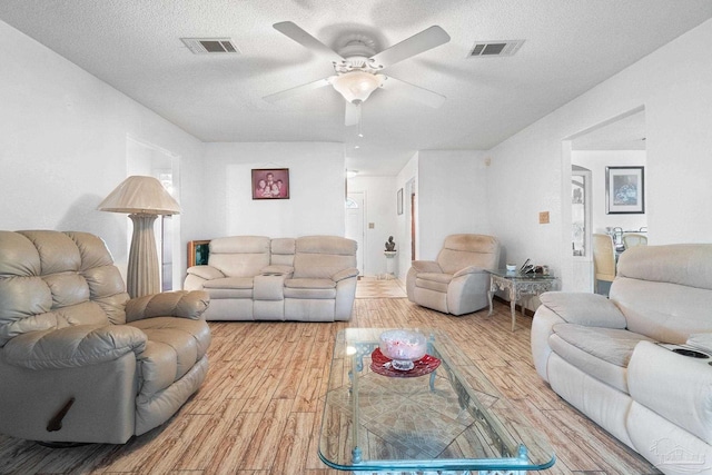 living room with ceiling fan, light wood-type flooring, and a textured ceiling