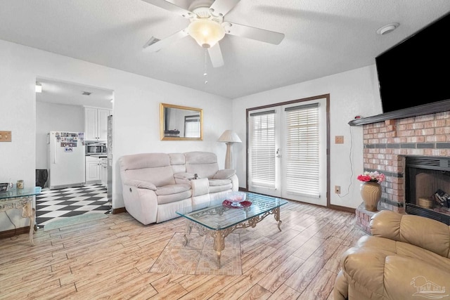 living room with ceiling fan, light wood-type flooring, a textured ceiling, and a fireplace