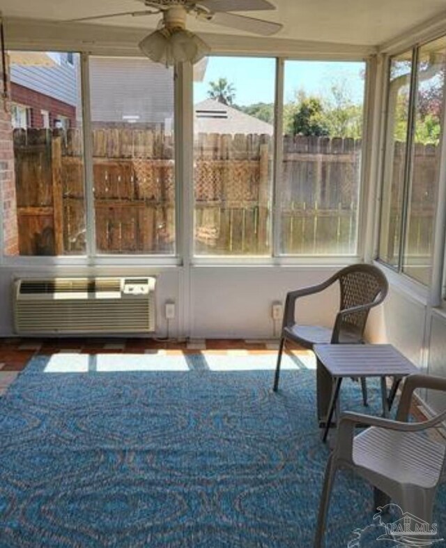 sunroom featuring a wall unit AC, a ceiling fan, and a wealth of natural light