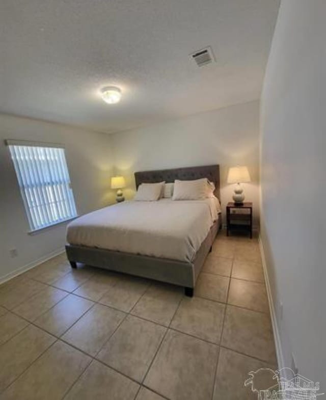 bedroom featuring light tile patterned floors, a textured ceiling, visible vents, and baseboards