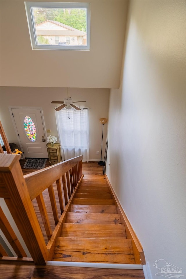 staircase featuring a towering ceiling, baseboards, and wood finished floors