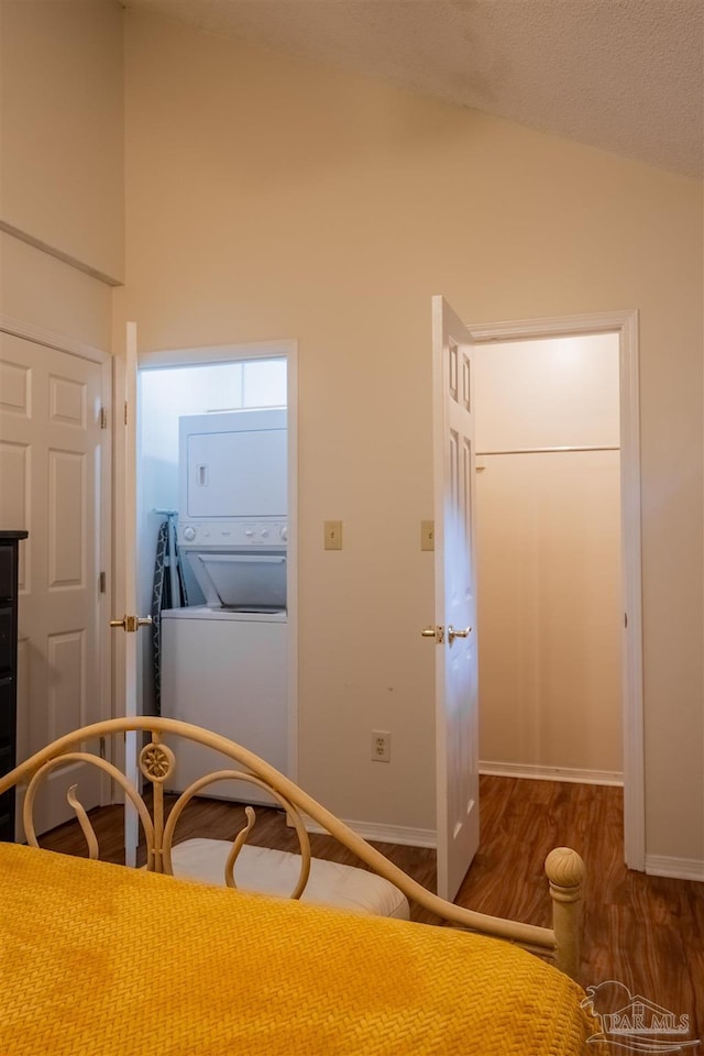 unfurnished bedroom featuring dark wood-style floors, baseboards, high vaulted ceiling, and stacked washing maching and dryer