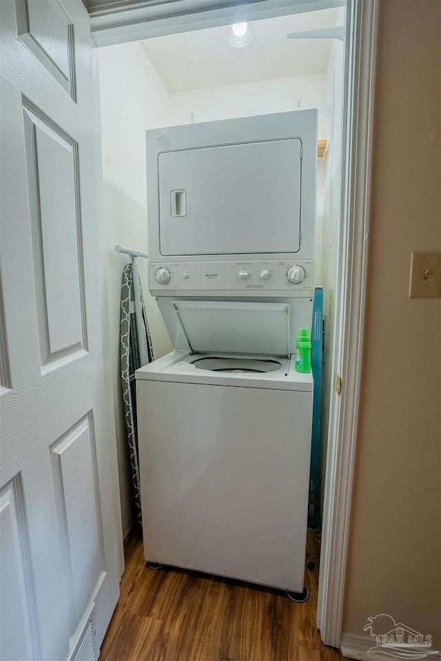 laundry room with stacked washer / drying machine, laundry area, and light wood-style flooring