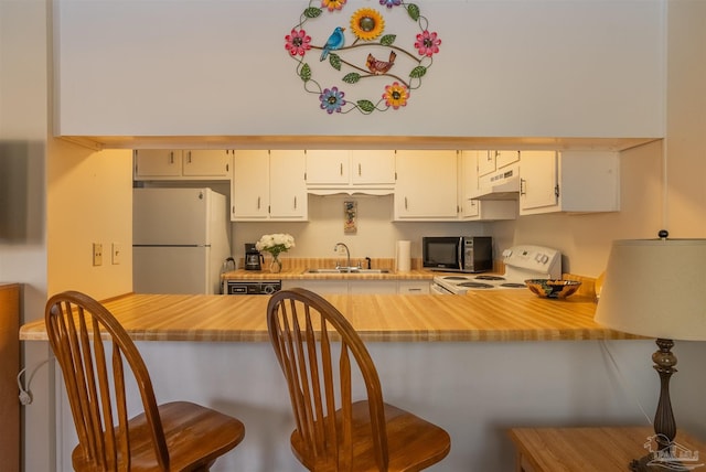 kitchen featuring light countertops, a sink, white appliances, under cabinet range hood, and a kitchen bar