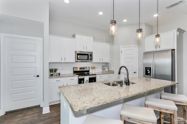 kitchen with decorative light fixtures, sink, stainless steel appliances, and an island with sink