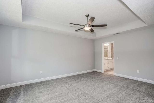 carpeted spare room featuring a textured ceiling, a tray ceiling, and ceiling fan