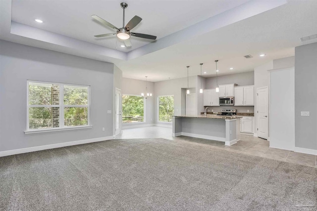 unfurnished living room with light carpet, ceiling fan with notable chandelier, and a raised ceiling