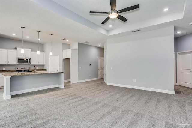 unfurnished living room featuring sink, light carpet, a tray ceiling, and ceiling fan