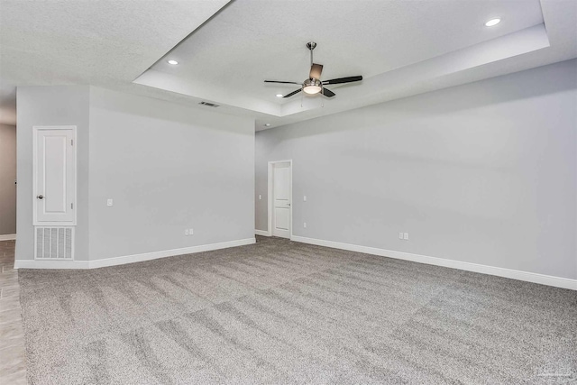 empty room featuring ceiling fan, light carpet, a textured ceiling, and a tray ceiling