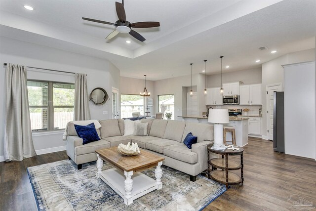 living room featuring ceiling fan with notable chandelier, a raised ceiling, and dark hardwood / wood-style floors