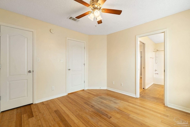 unfurnished bedroom featuring ceiling fan, ensuite bathroom, a textured ceiling, and light wood-type flooring