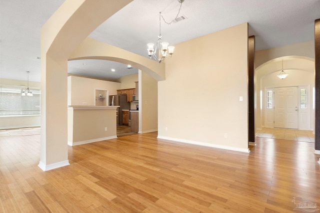 unfurnished living room featuring an inviting chandelier and light wood-type flooring