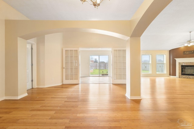 unfurnished living room with a tiled fireplace, ceiling fan, lofted ceiling, and light wood-type flooring