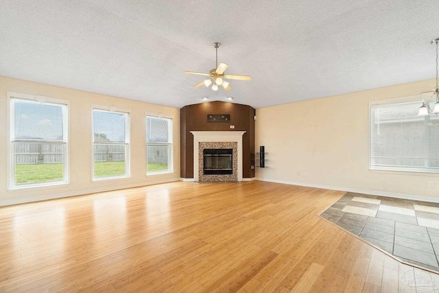 unfurnished living room featuring vaulted ceiling, light hardwood / wood-style flooring, a textured ceiling, a high end fireplace, and ceiling fan with notable chandelier