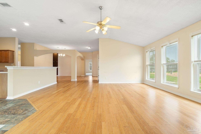 unfurnished living room featuring ceiling fan with notable chandelier, a wealth of natural light, a textured ceiling, and light wood-type flooring