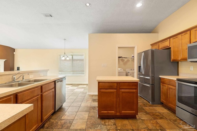 kitchen with sink, appliances with stainless steel finishes, a center island, separate washer and dryer, and decorative light fixtures