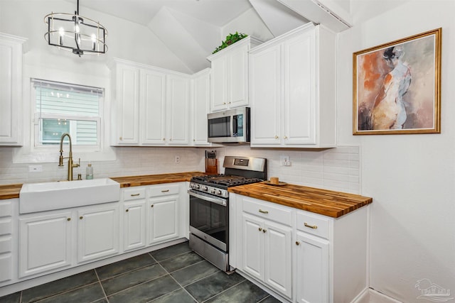 kitchen featuring white cabinetry, wood counters, stainless steel appliances, dark tile patterned flooring, and sink