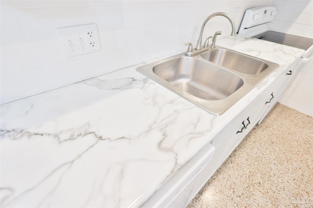 interior details with white cabinetry, sink, and light stone counters