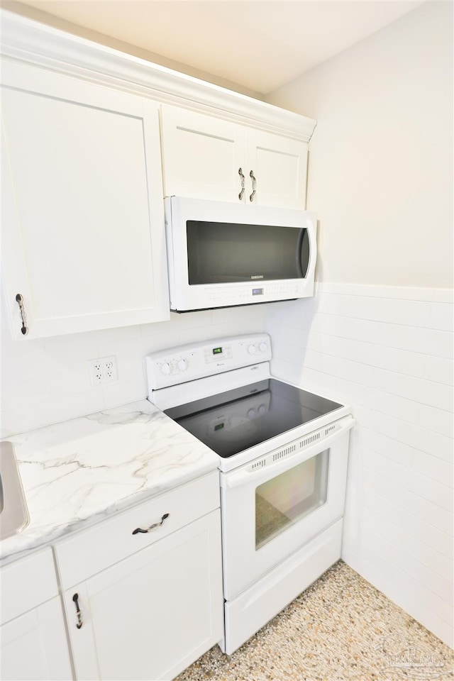 kitchen featuring tile walls, white appliances, white cabinetry, and light stone countertops