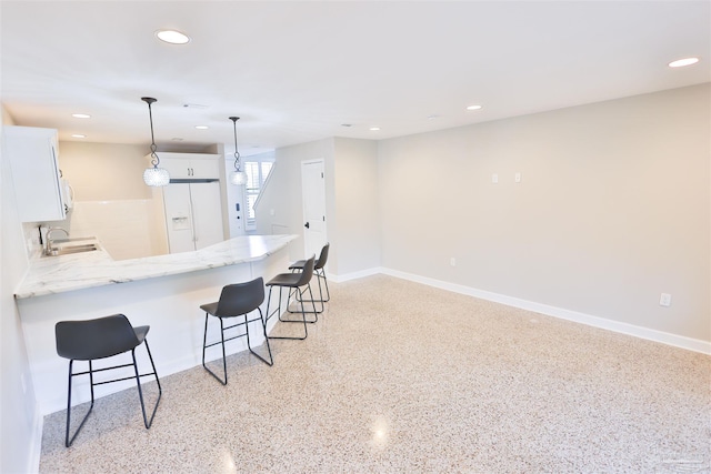 kitchen featuring white fridge with ice dispenser, decorative light fixtures, sink, white cabinetry, and kitchen peninsula