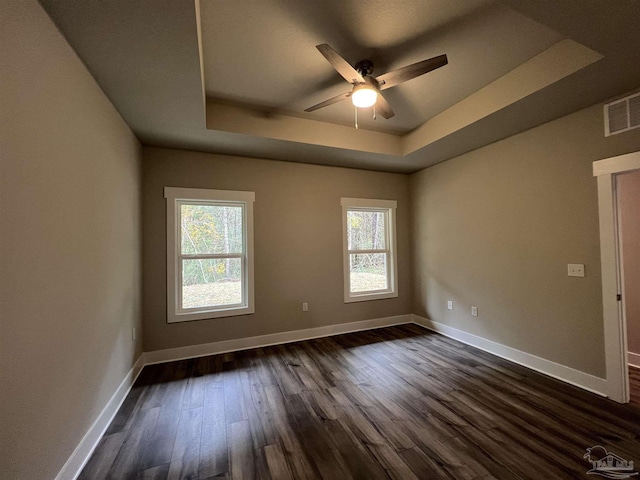 spare room with dark hardwood / wood-style floors, a raised ceiling, plenty of natural light, and ceiling fan