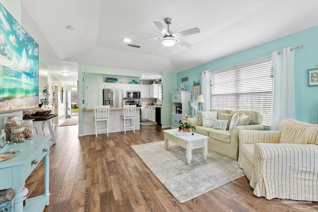 living room with a raised ceiling, dark hardwood / wood-style flooring, ceiling fan, and plenty of natural light