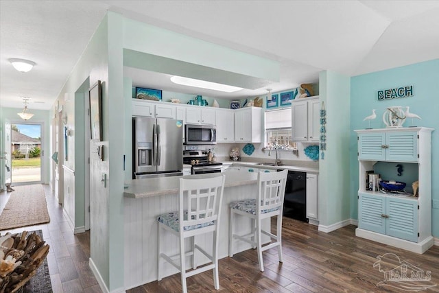 kitchen with sink, stainless steel appliances, dark hardwood / wood-style flooring, a breakfast bar area, and white cabinets