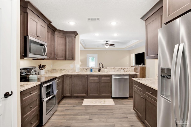 2956 N 17th Ave, Milton, FL 32583 - kitchen featuring appliances with stainless steel finishes, a tray ceiling, a peninsula, a sink, and light wood-type flooring